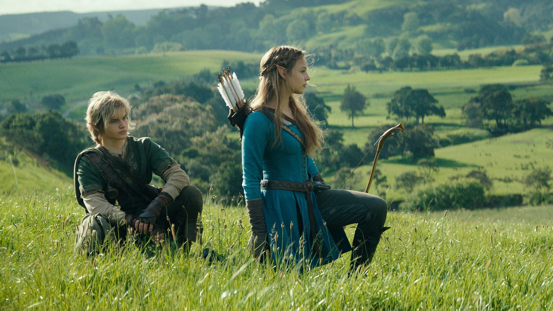 Two young people in fantasy attire, one resembling Link and the other an elf with a bow and quiver, are in a sunny, grassy field with green hills.