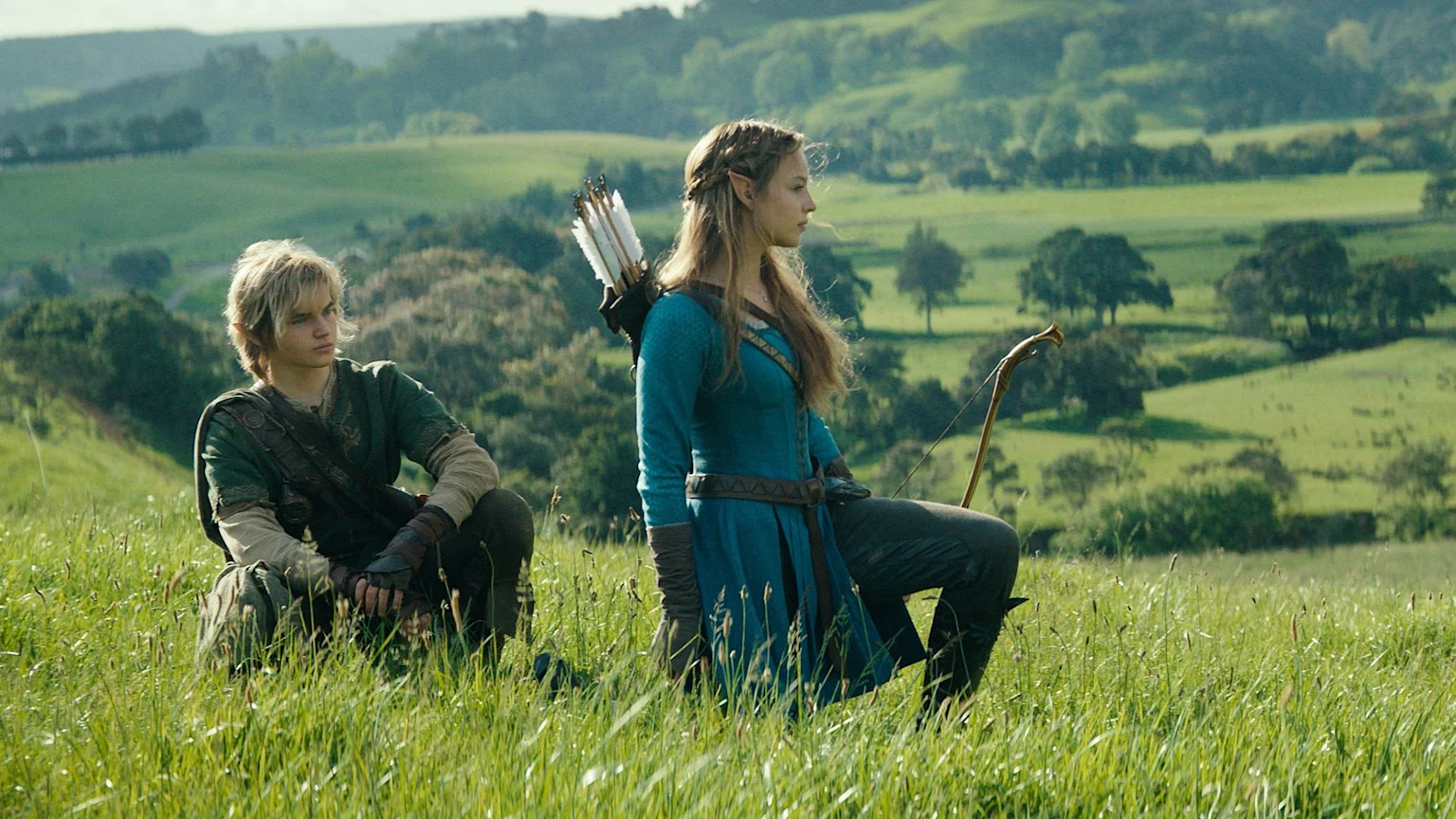 Two young people in fantasy attire, one resembling Link and the other an elf with a bow and quiver, are in a sunny, grassy field with green hills.