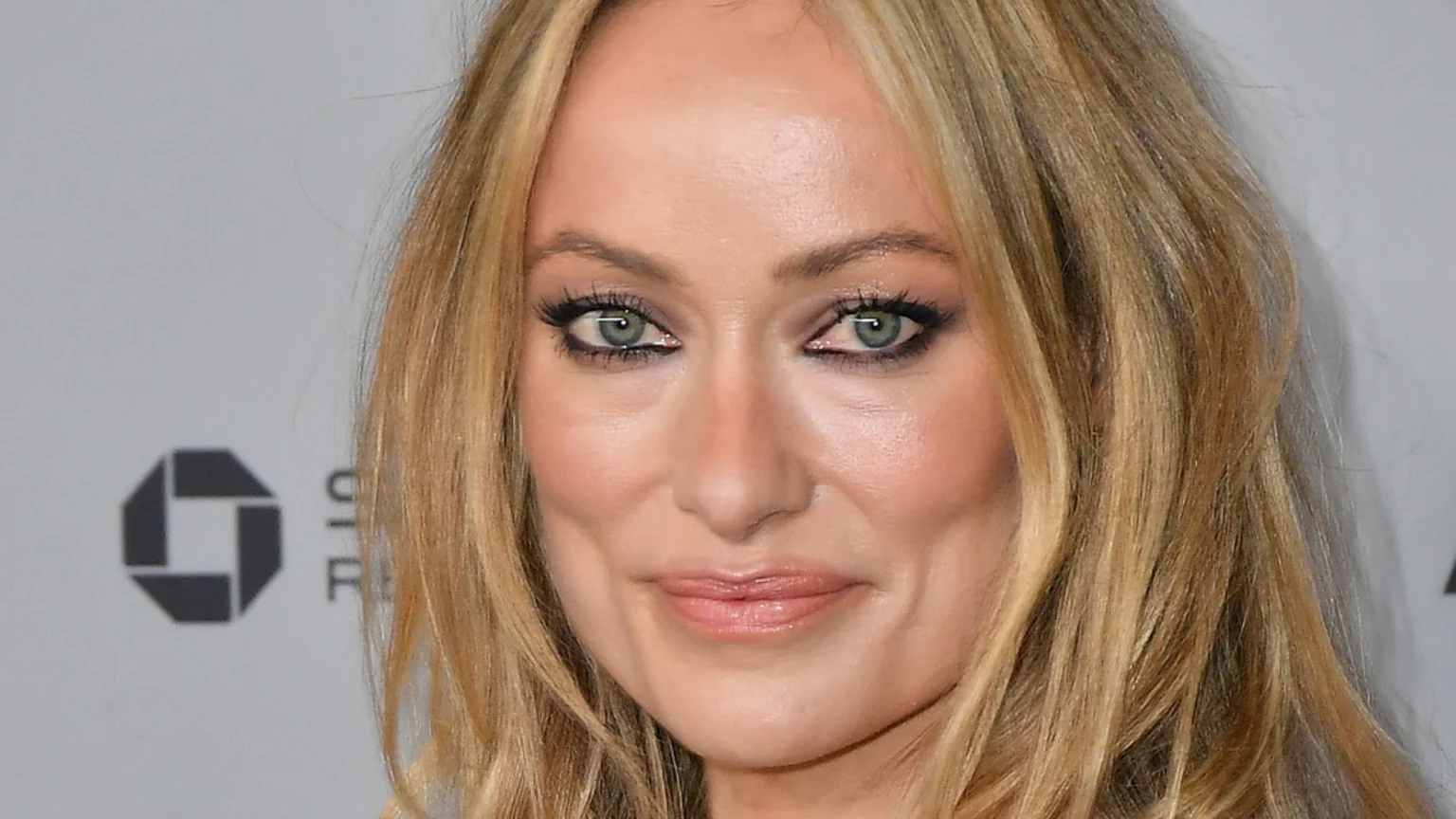 Close-up of Olivia Wilde with blonde hair and green eyes, subtly smiling directly at the camera.