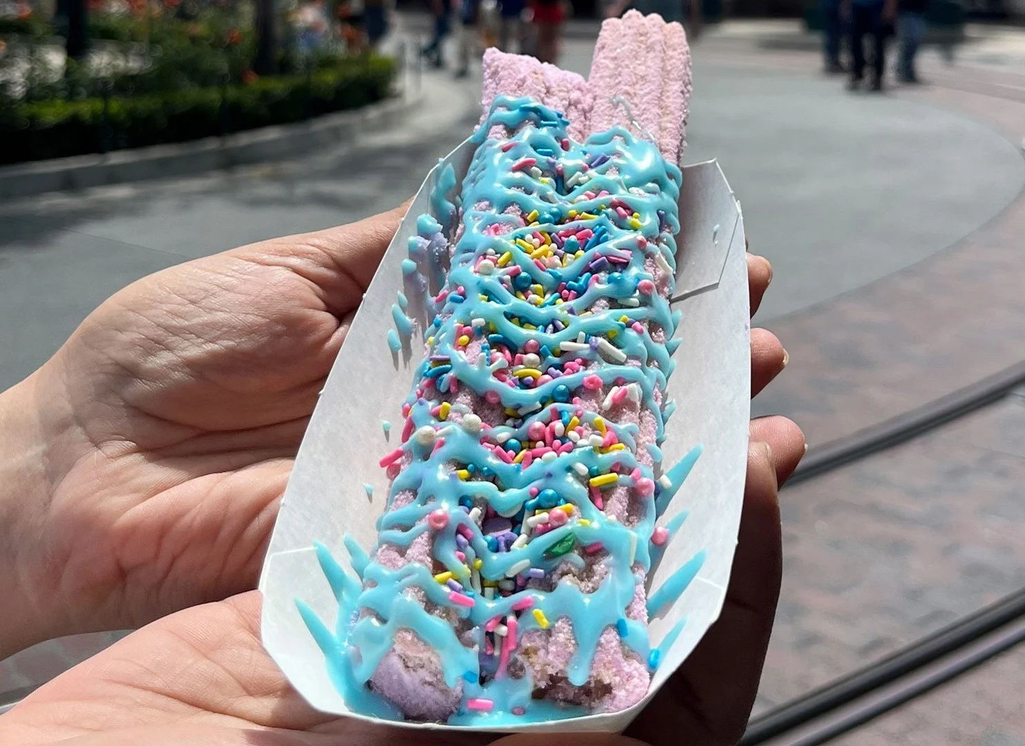 Two Ube (purple yam) sugar coated Churros with blue icing drizzled over top and rainbow sprinkles.