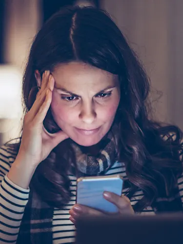 Woman looking at her cell phone screen as if she's asked it a question and reading the answer.