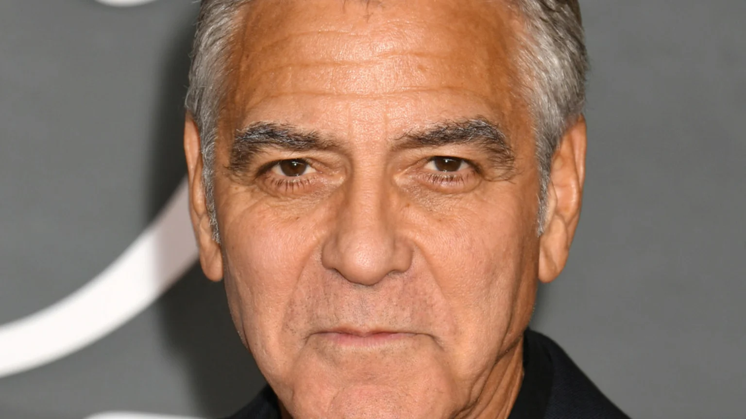Close-up of actor George Clooney looking directly at the camera with a neutral expression against a grey background.