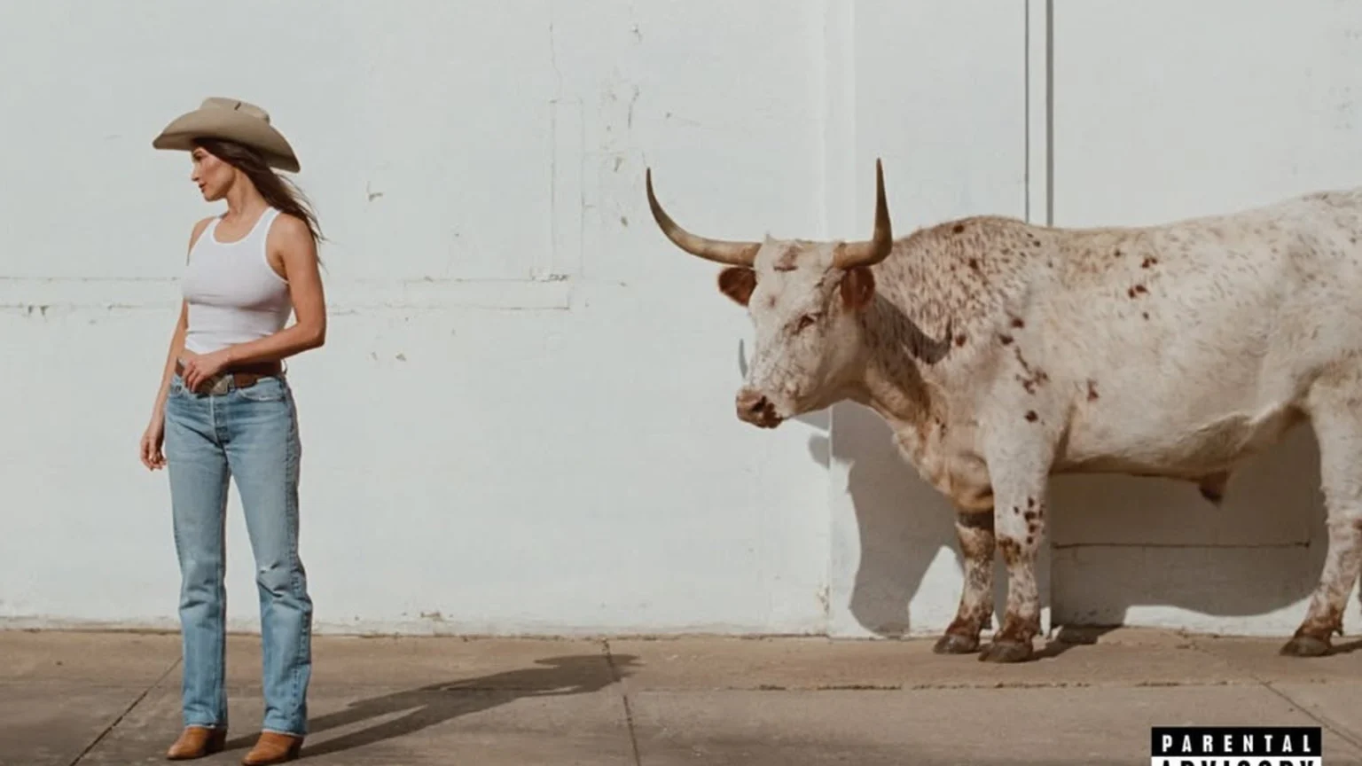 A woman in a cowboy hat, white tank top, and jeans stands on the left, looking away from a white bull with brown spots and horns on the right, both against a white wall with a Parental Advisory label bottom right.