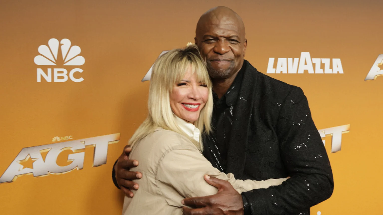 Rebecca King-Crews and Terry Crews embrace and smile on a yellow backdrop with NBC, AGT, and Lavazza logos.