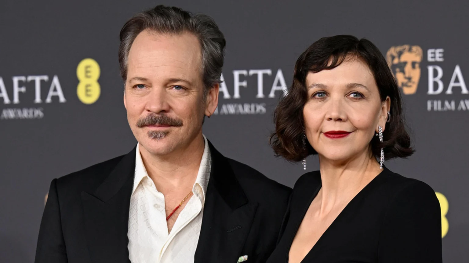 A man with facial hair and a woman with short dark hair and red lipstick pose side-by-side against a black background with BAFTA logos.