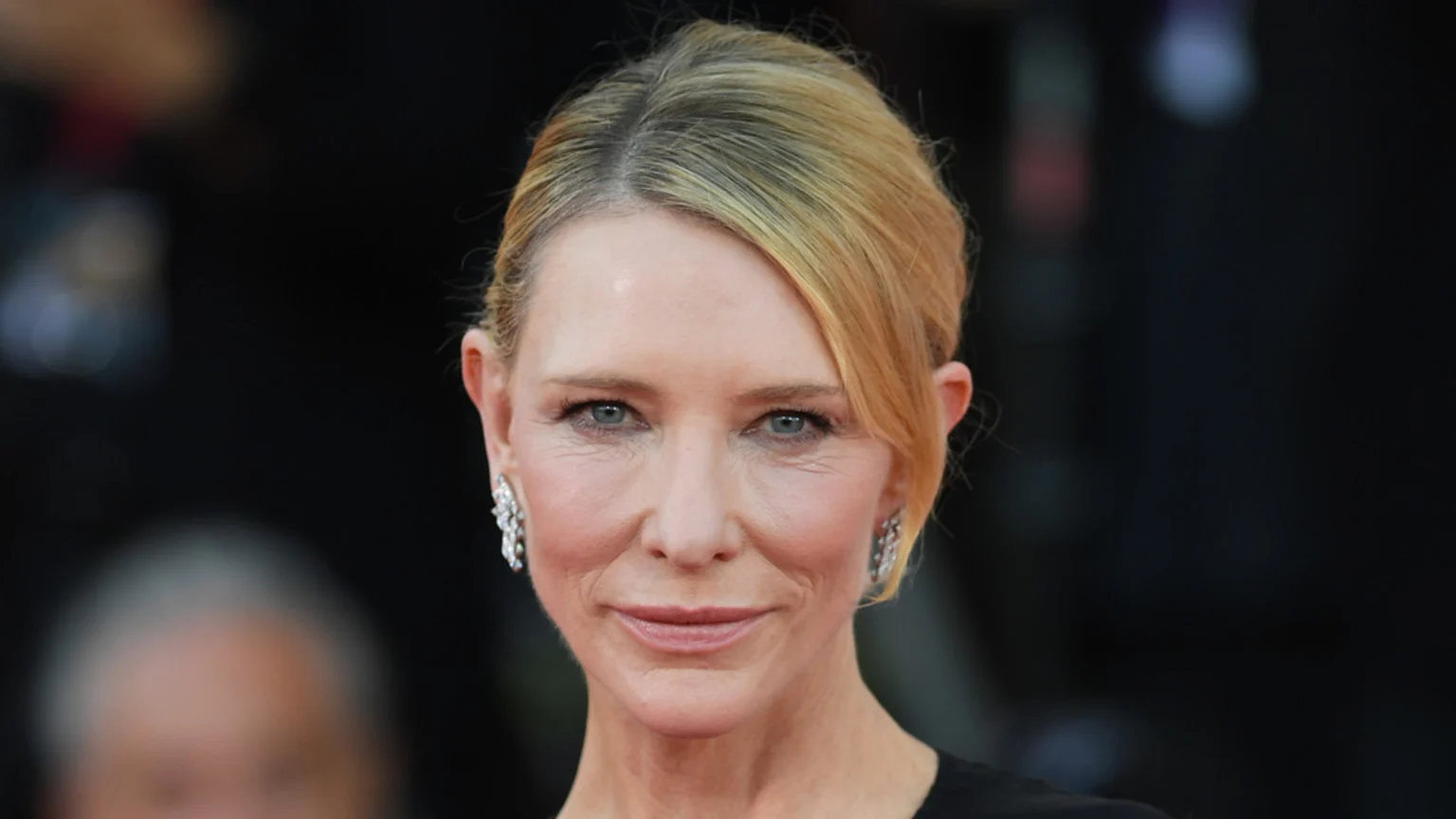 A close-up shot of actress Cate Blanchett, with blonde hair pulled back, wearing diamond earrings and looking directly at the camera with a gentle expression.