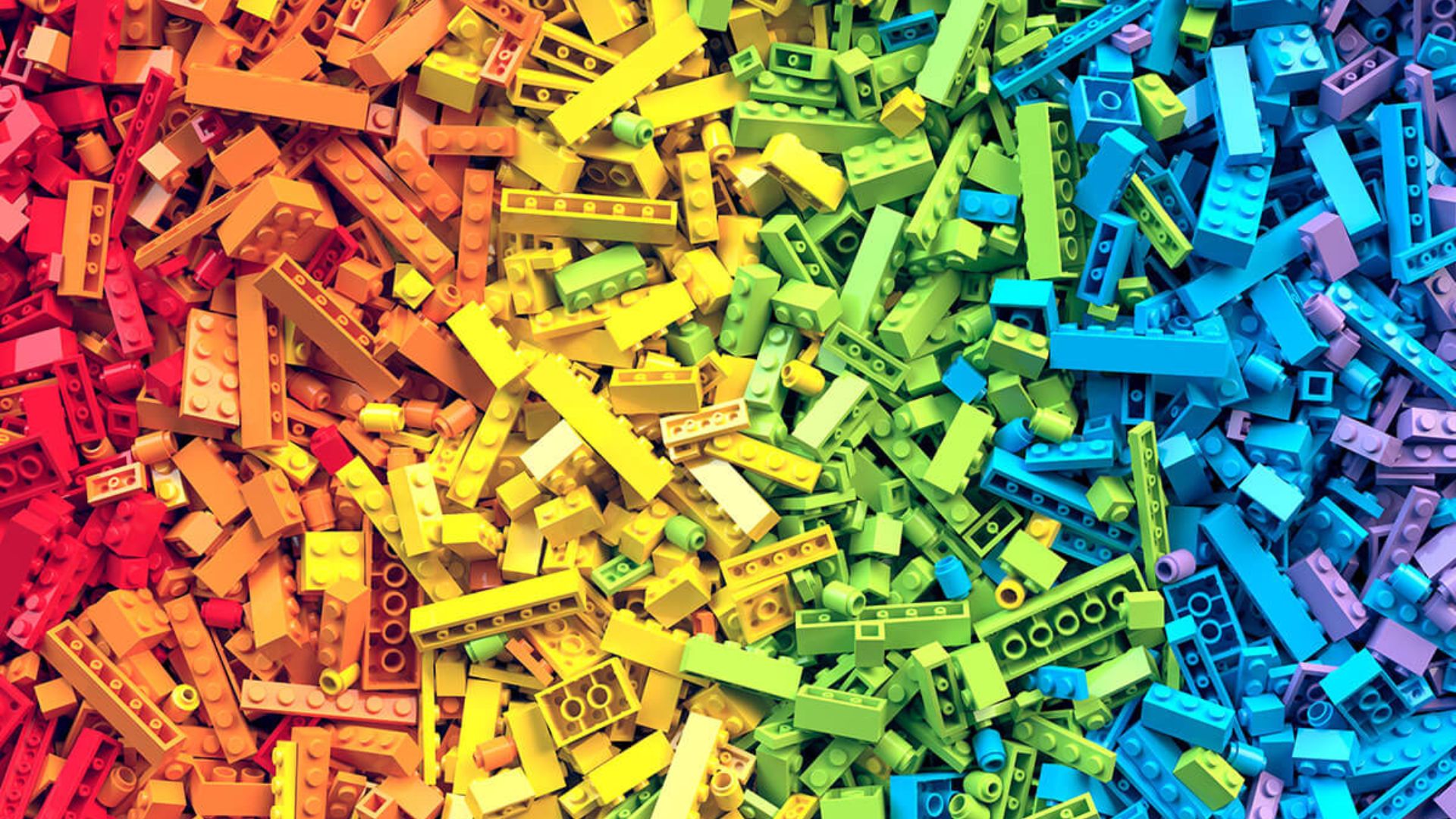 A vibrant pile of interlocking plastic building bricks, color-sorted in a gradient from red through green to purple.