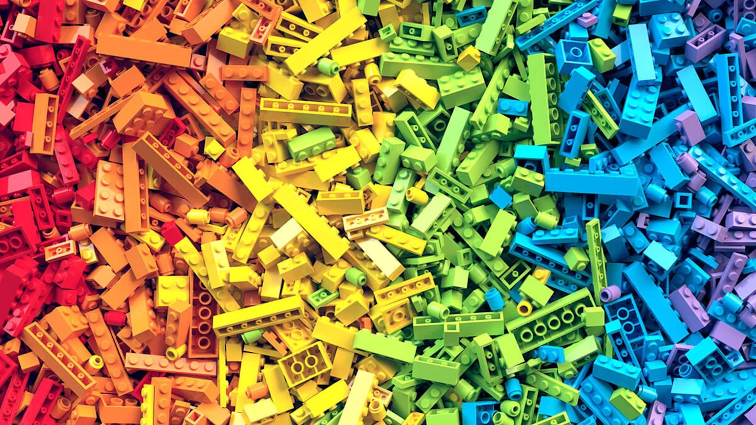 A vibrant pile of interlocking plastic building bricks, color-sorted in a gradient from red through green to purple.