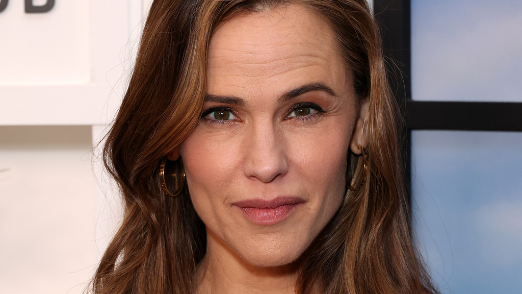 Close-up of Jennifer Garner looking directly at the camera, with brown wavy hair framing her face, gold hoop earrings, and visible forehead wrinkles.