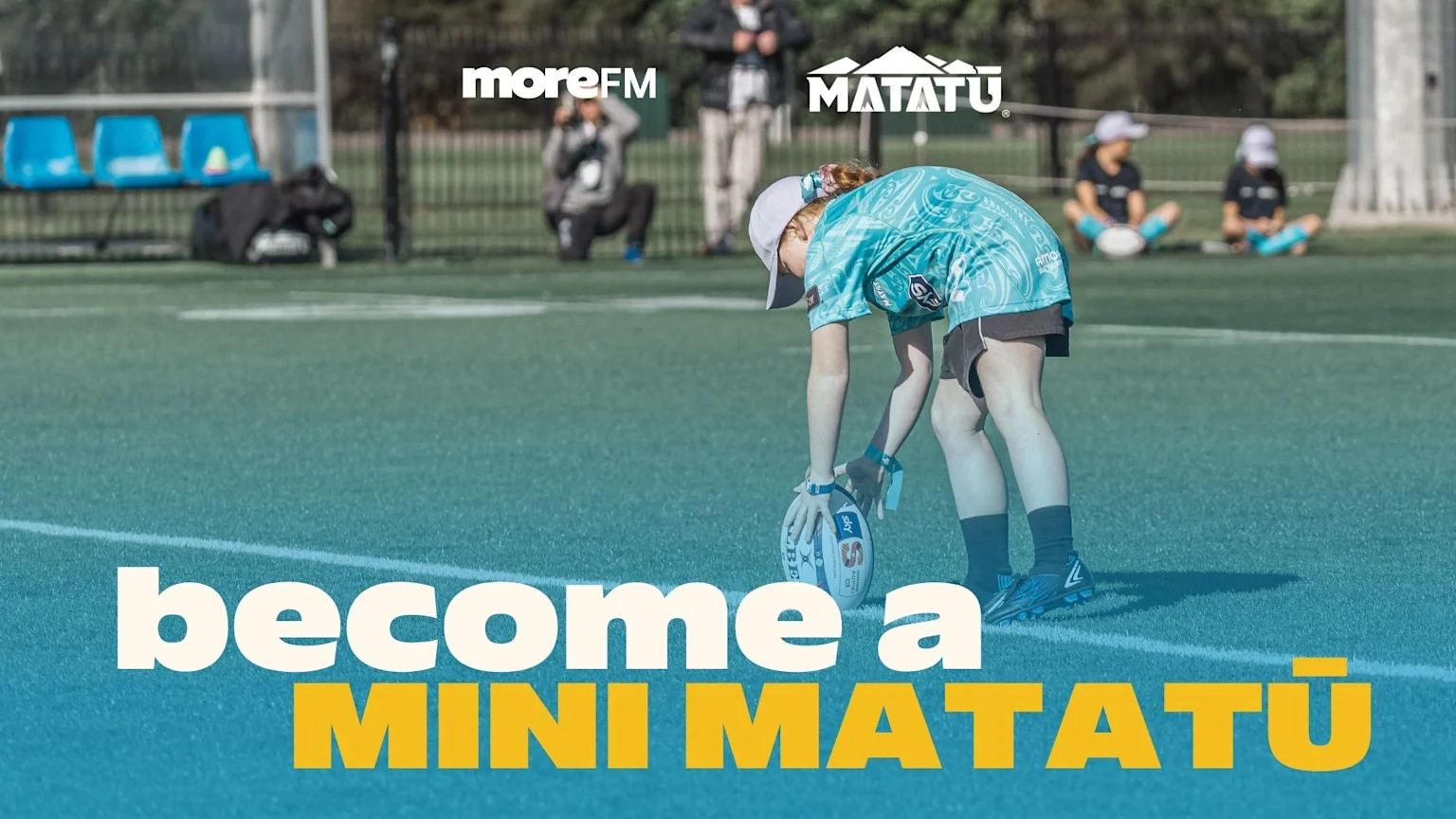 A young person in a teal rugby jersey places a ball on a green field, with "moreFM" and "MATATŪ" logos at the top, and "become a MINI MATATŪ" text overlaid at the bottom.