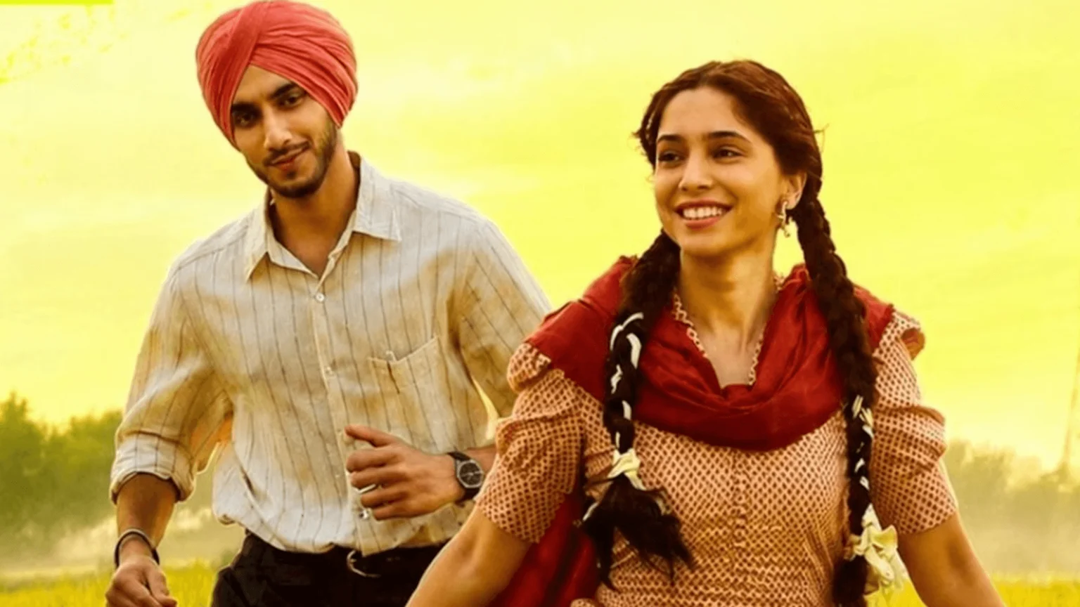A smiling young man in a red turban and a joyful young woman with braided hair walk together against a vibrant yellow background.