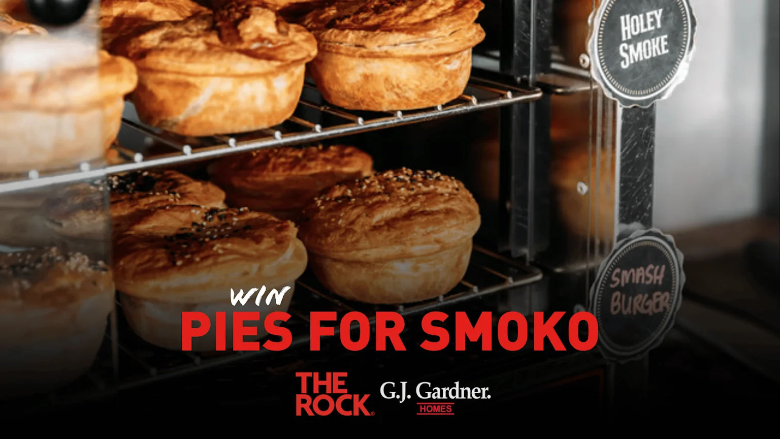 A display case shows shelves filled with many golden-brown baked pies, some topped with seeds, alongside signs for "Holey Smoke" and "Smash Burger," with text "WIN PIES FOR SMOKO" and sponsor logos.