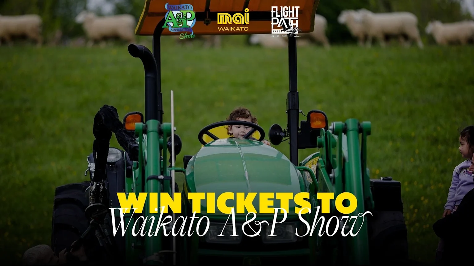 A child sits in a green tractor in a field with sheep and another child, with logos for Waikato A&P Show, Mai Waikato, and Flight Path Entertainment visible at the top.