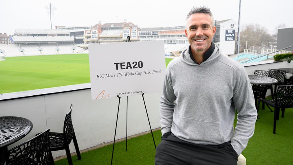 A smiling man in a grey hoodie stands beside a sign for the ICC Men's T20 World Cup 2026 Final, overlooking a cricket stadium with "THE OVAL" visible in the background.
