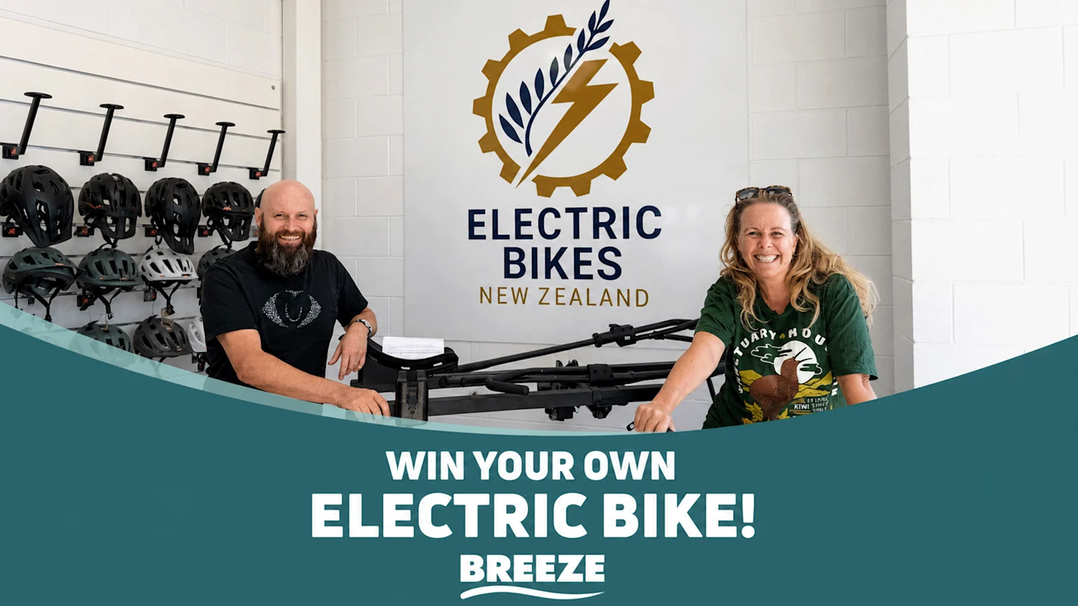 A smiling man and woman stand in an electric bike shop with helmets, an "Electric Bikes New Zealand" sign, and text announcing "WIN YOUR OWN ELECTRIC BIKE!".
