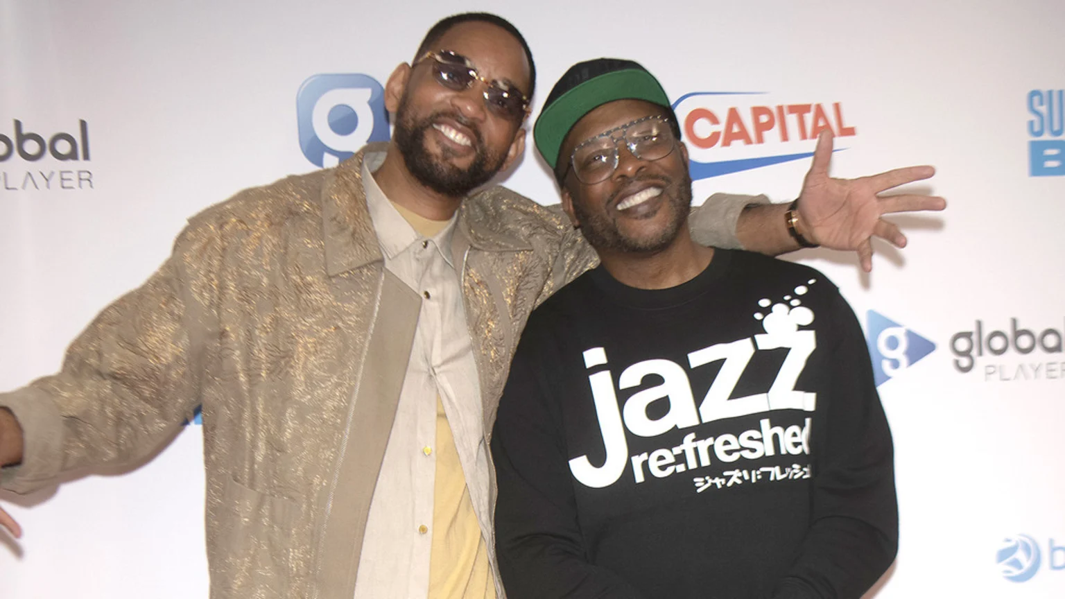 Will Smith, in a gold jacket and sunglasses, stands next to DJ Jazzy Jeff, in a black cap and "jazz re:freshed" shirt, both smiling at the camera against a white backdrop with logos.
