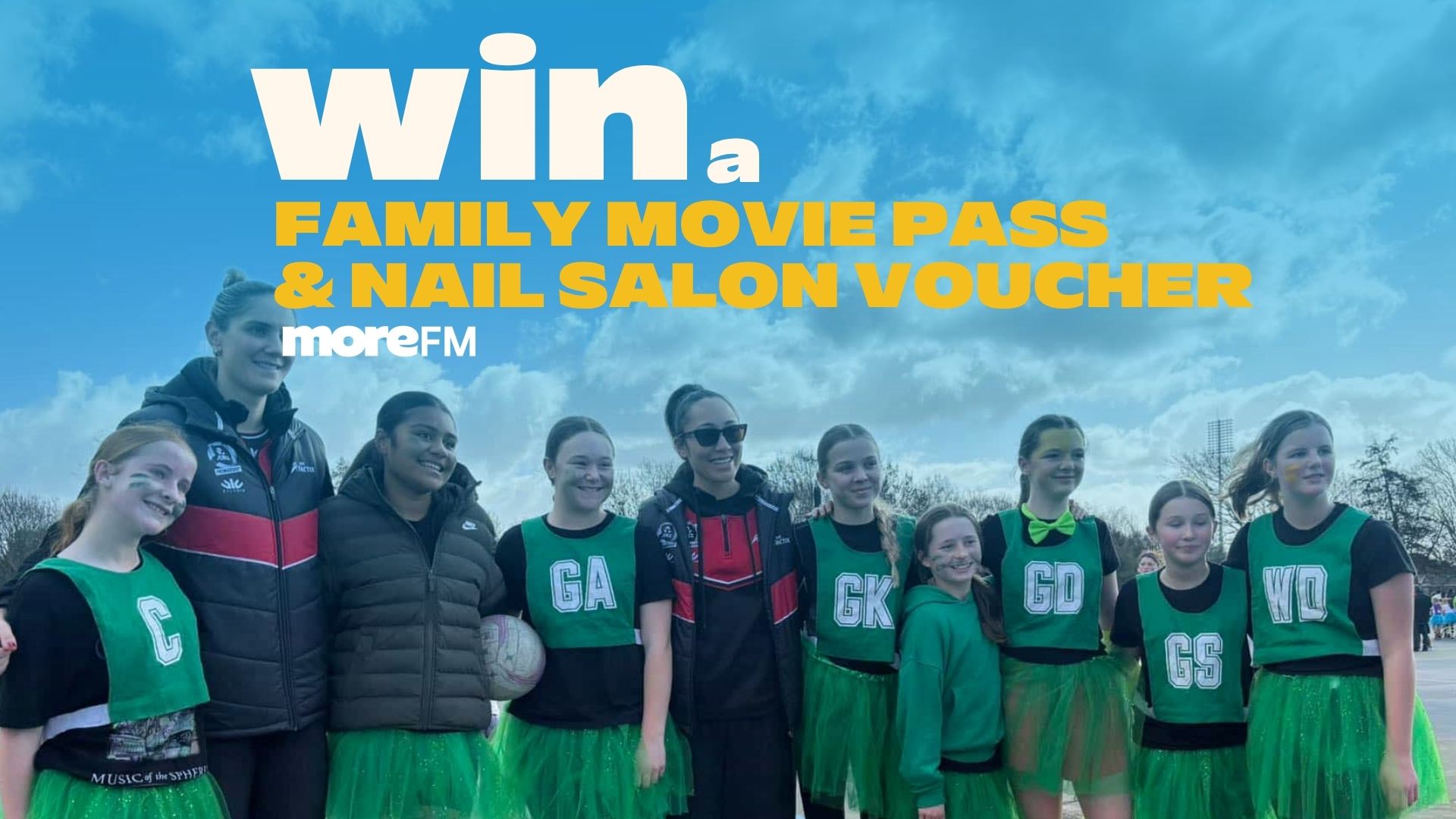A group of young girls in green netball uniforms with face paint and two adult women, under a cloudy sky, with a promotional text overlay: "Win a FAMILY MOVIE PASS & NAIL SALON VOUCHER moreFM".