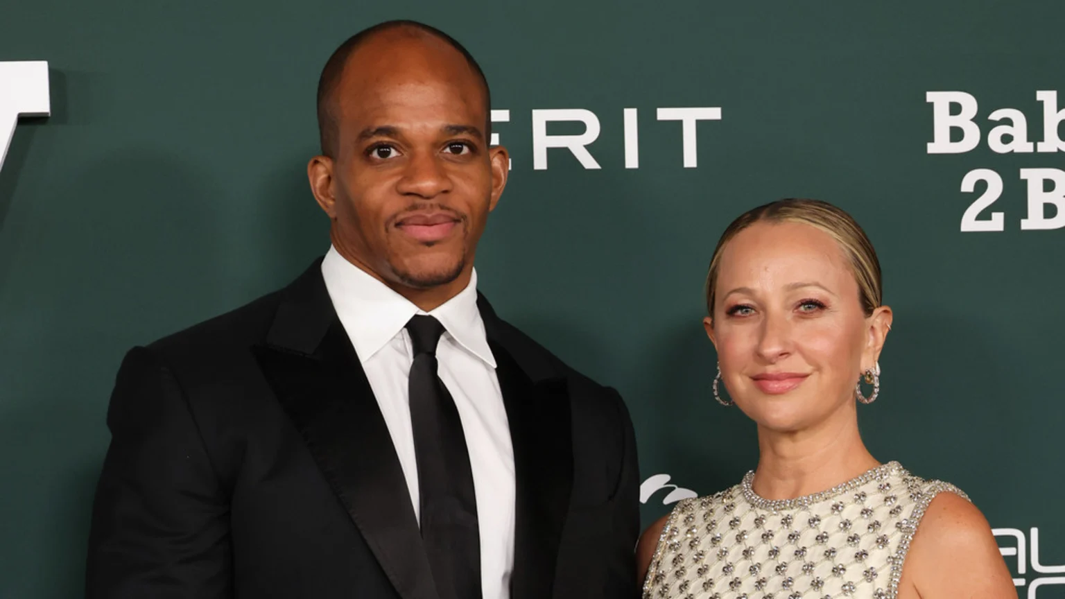 A man in a black suit and a woman in an embellished dress stand side-by-side, smiling against a dark green background with white text.