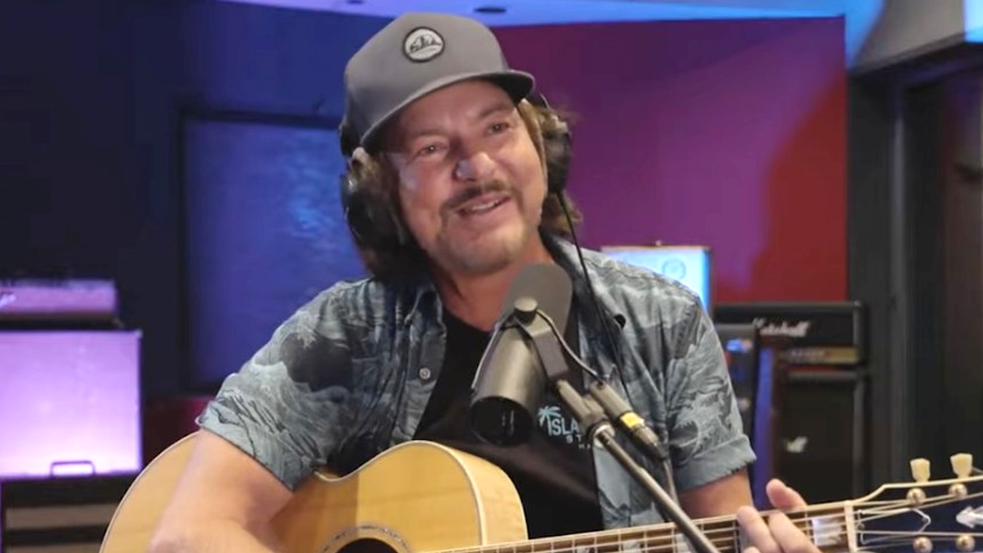 A smiling man with a beard in a black suit stands next to a smiling woman with her hair up, wearing a black top and necklace, against a dark background with large white and gold letters.