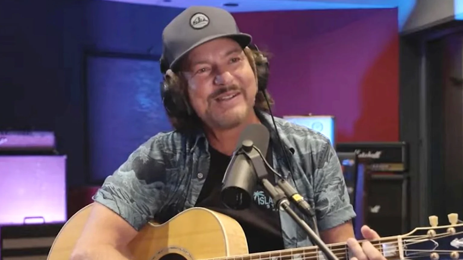 A smiling man with a beard in a black suit stands next to a smiling woman with her hair up, wearing a black top and necklace, against a dark background with large white and gold letters.