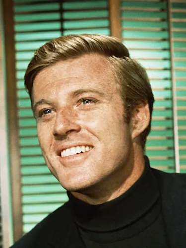 Robert Redford smiling in front of teal blinds