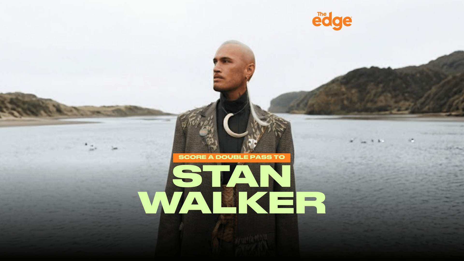 A man identified as Stan Walker, with light hair and a C-shaped necklace, stands in a textured jacket before a body of water and hills, with text "SCORE A DOUBLE PASS TO STAN WALKER" and "The edge" logo.