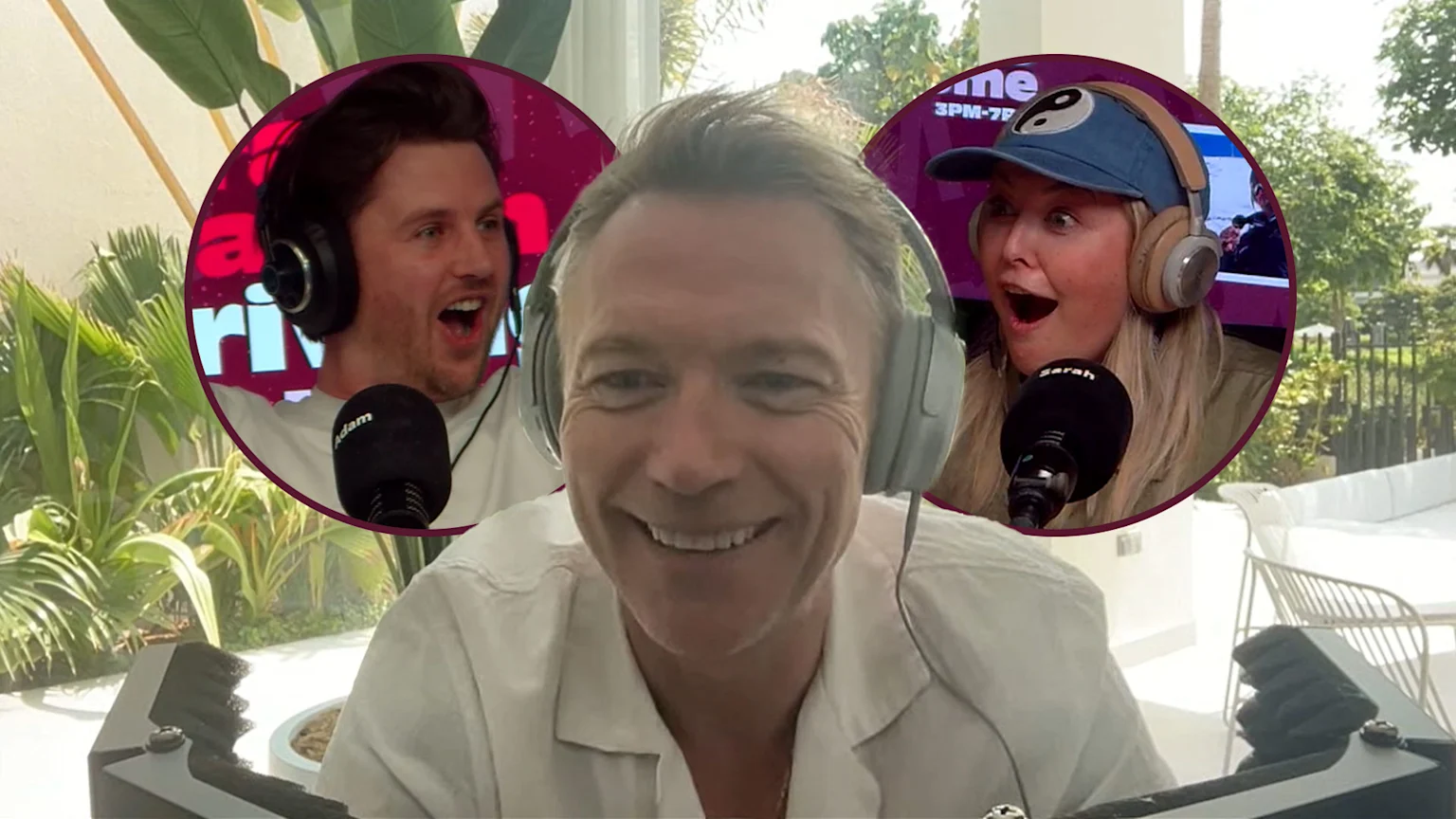 Ronan Keating smiles wearing headphones on a video call, flanked by circular insets of an excited man named Adam and an excited woman named Sarah, both with headphones and microphones, against a bright, lush outdoor background.