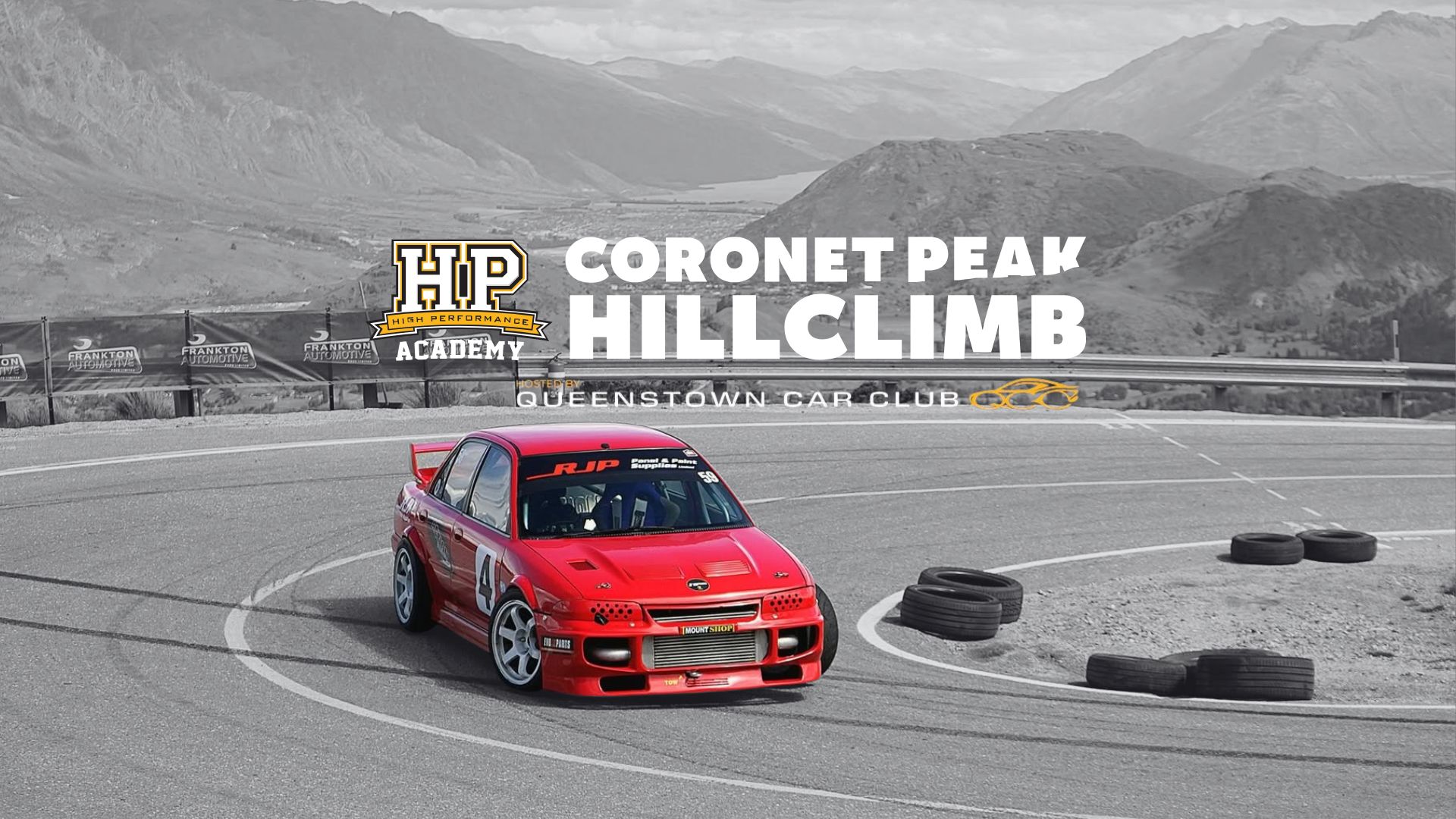 A vibrant red race car with number 4 rounds a turn on a paved mountain road, flanked by tire barriers, under a grayscale landscape and an overlay for the Coronet Peak Hillclimb.
