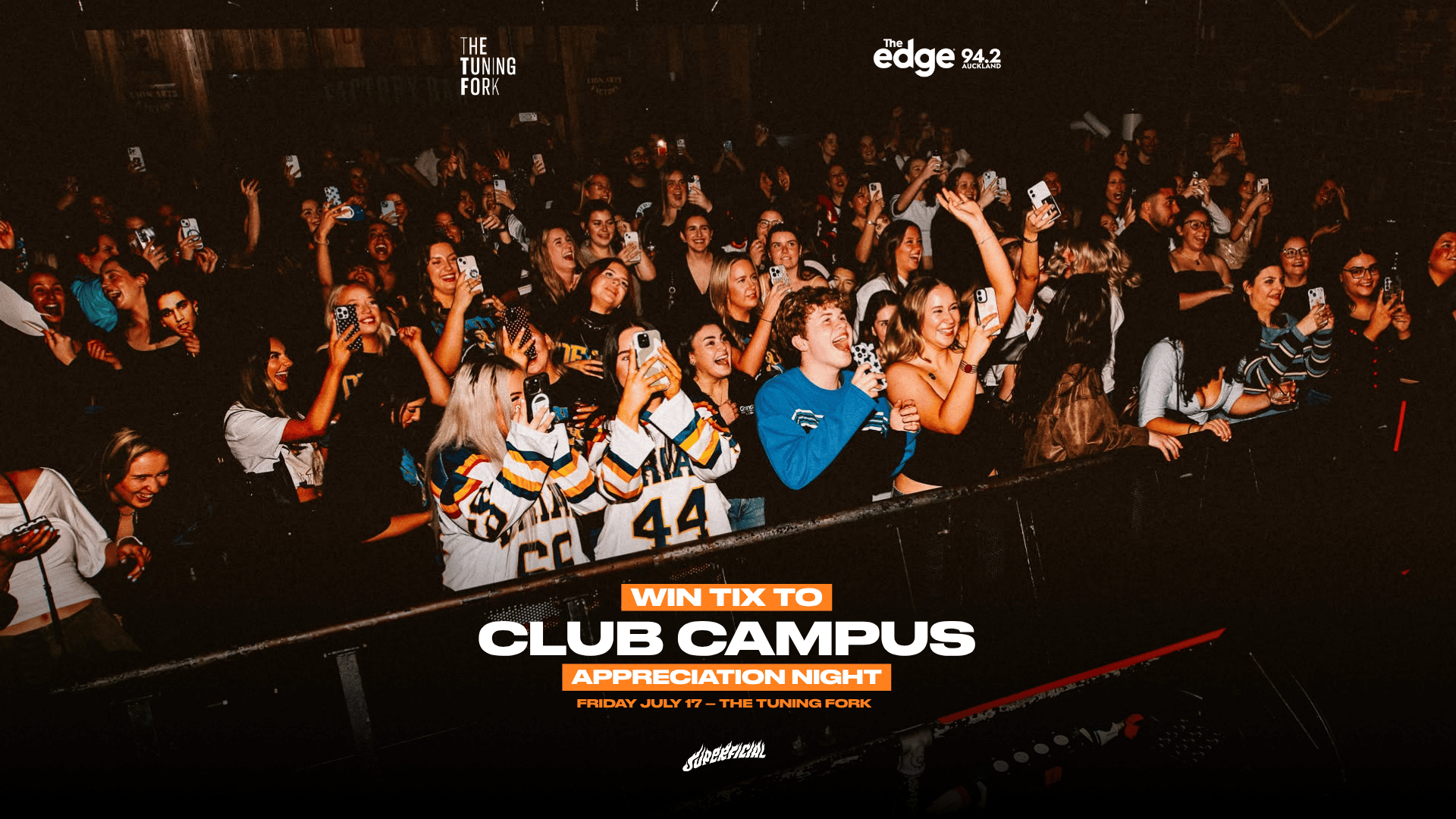 An enthusiastic crowd of young adults at a dimly lit club or concert, many smiling, laughing, and holding up their phones, with promotional text overlaid.