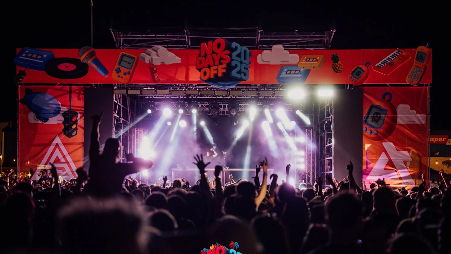A lively outdoor concert at night, showing a stage with bright lights, a crowd of people with hands raised, and a large banner reading "NO DAYS OFF 20 25" with retro items.