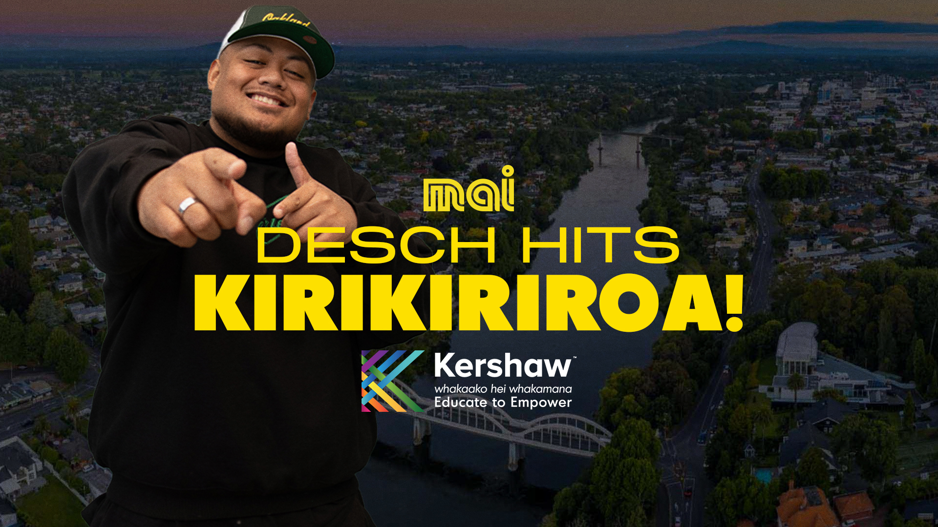 A smiling man in a green cap points at the viewer, overlaid on an aerial view of a city with a river and a bridge at dusk, with text "mai DESCH HITS KIRIKIRIROA!" and "Kershaw Educate to Empower."
