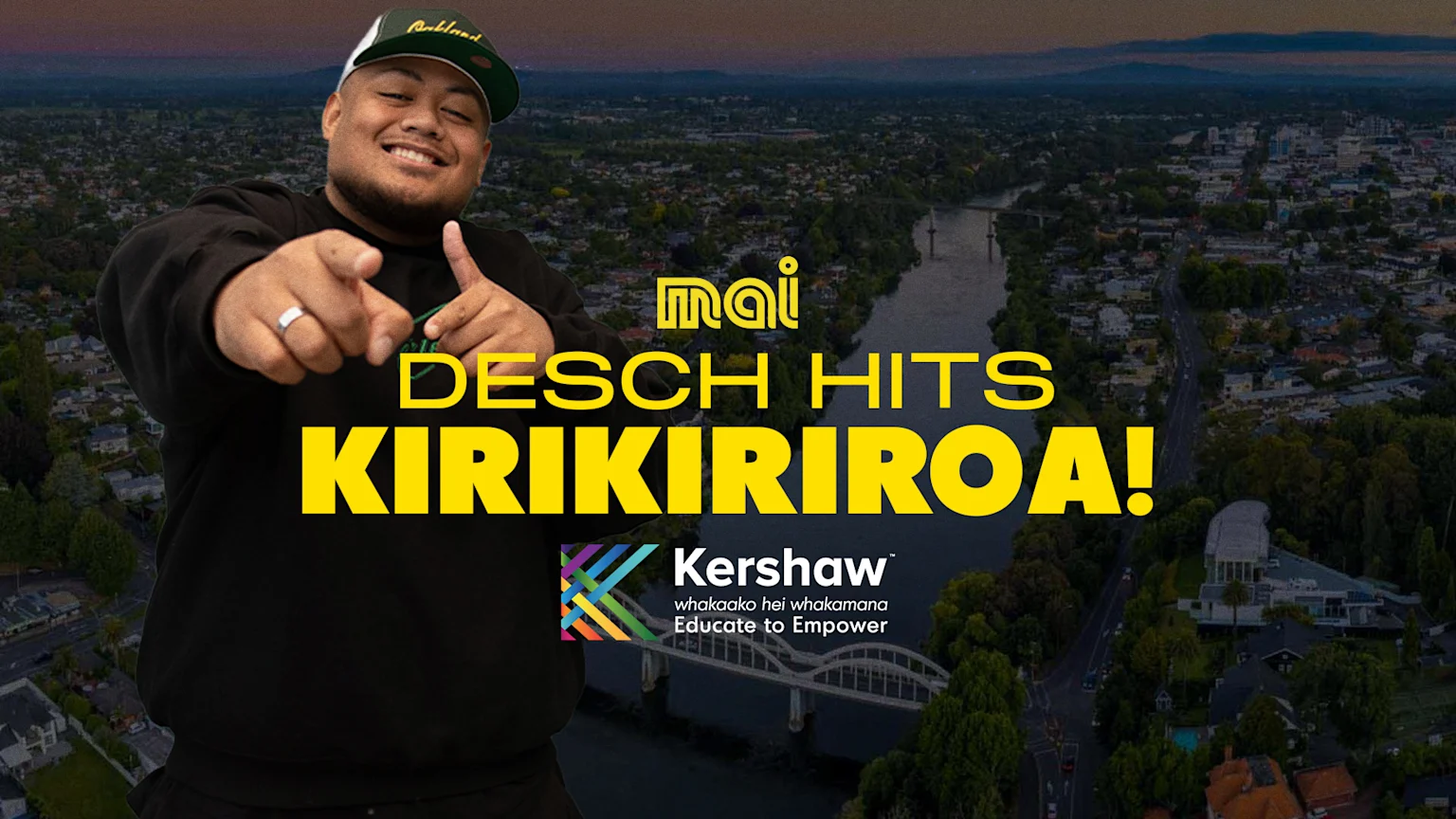 A smiling man in a green cap points at the viewer, overlaid on an aerial view of a city with a river and a bridge at dusk, with text "mai DESCH HITS KIRIKIRIROA!" and "Kershaw Educate to Empower."