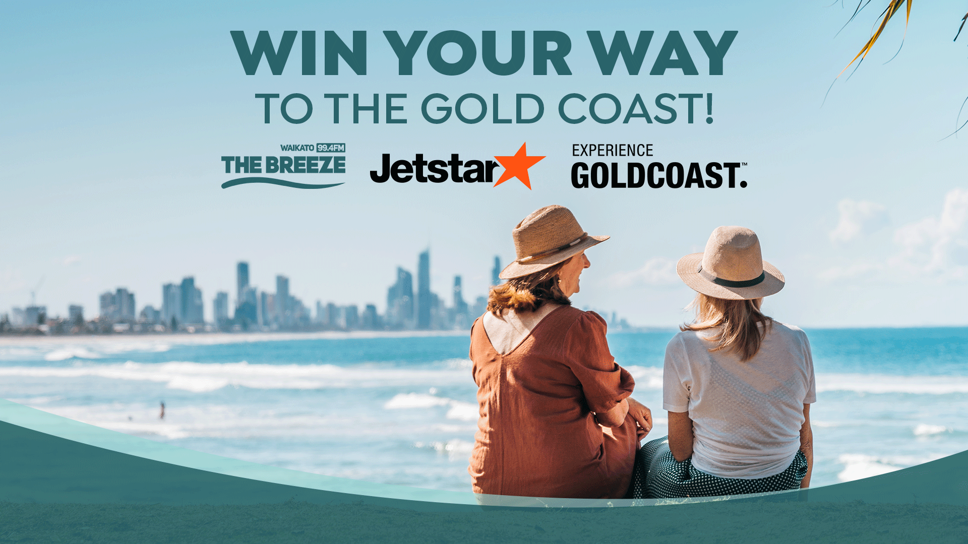 Two women in hats sit on a beach looking at the ocean and a distant city skyline, with text "WIN YOUR WAY TO THE GOLD COAST!" sponsored by The Breeze, Jetstar, and Experience Gold Coast.