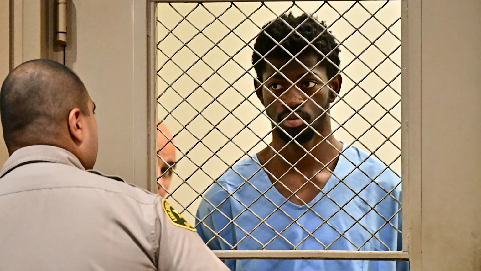 Lil Nas X behind barred door looking at an LA police officer.