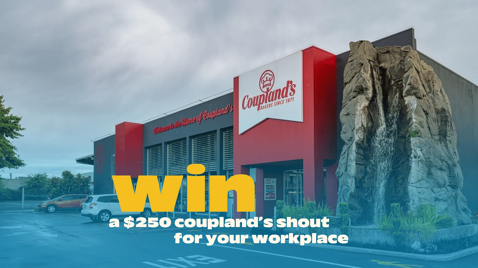 A Coupland's bakery building with red and grey walls, a large sign, and a rock waterfall, overlaid with text: 'Win a $250 Coupland's shout for your workplace'.