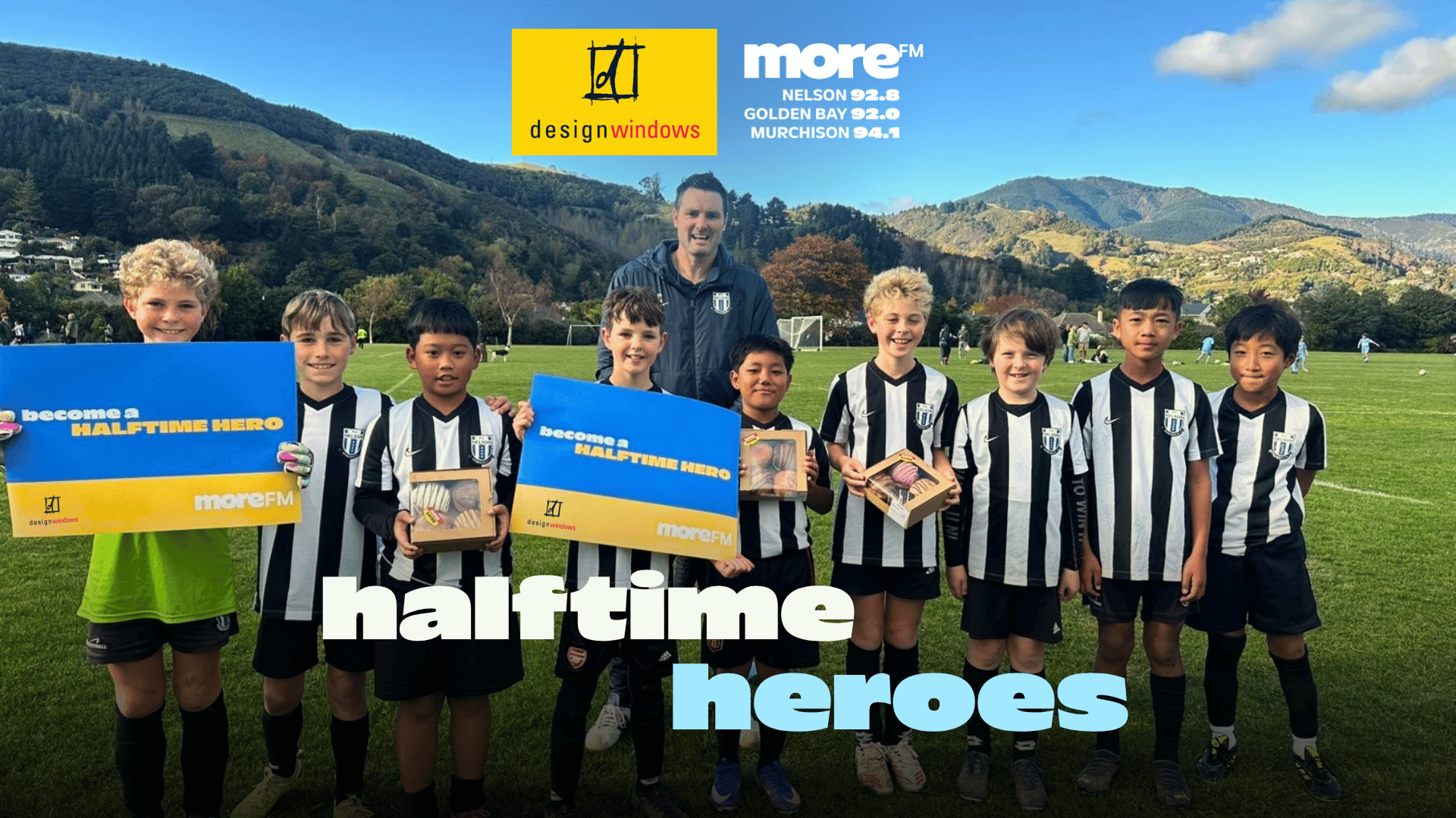 A group of smiling young soccer players and an adult on a field, some holding "HALFTIME HERO" signs with Design Windows and More FM branding, and large overlay text "halftime heroes."