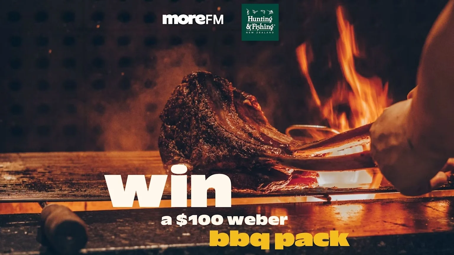 A large piece of meat grilling over open flames on a BBQ, being turned by tongs, with "moreFM" and "Hunting & Fishing New Zealand" logos and text "win a $100 weber bbq pack" visible.