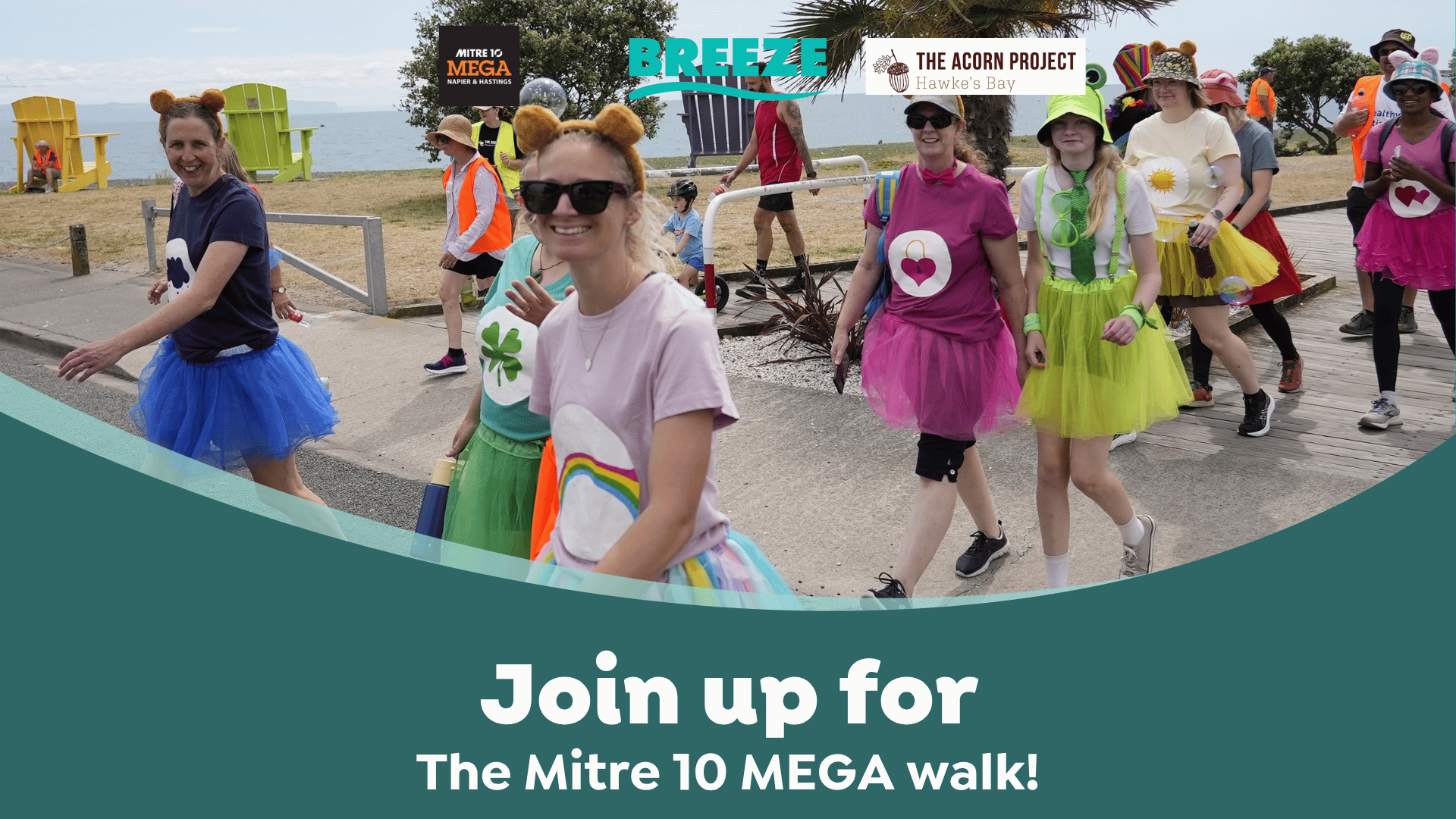 A group of smiling people, mostly women, walk outdoors dressed in colorful tutus and fun costumes, with event sponsors' logos and text "Join up for The Mitre 10 MEGA walk!" overlaid.