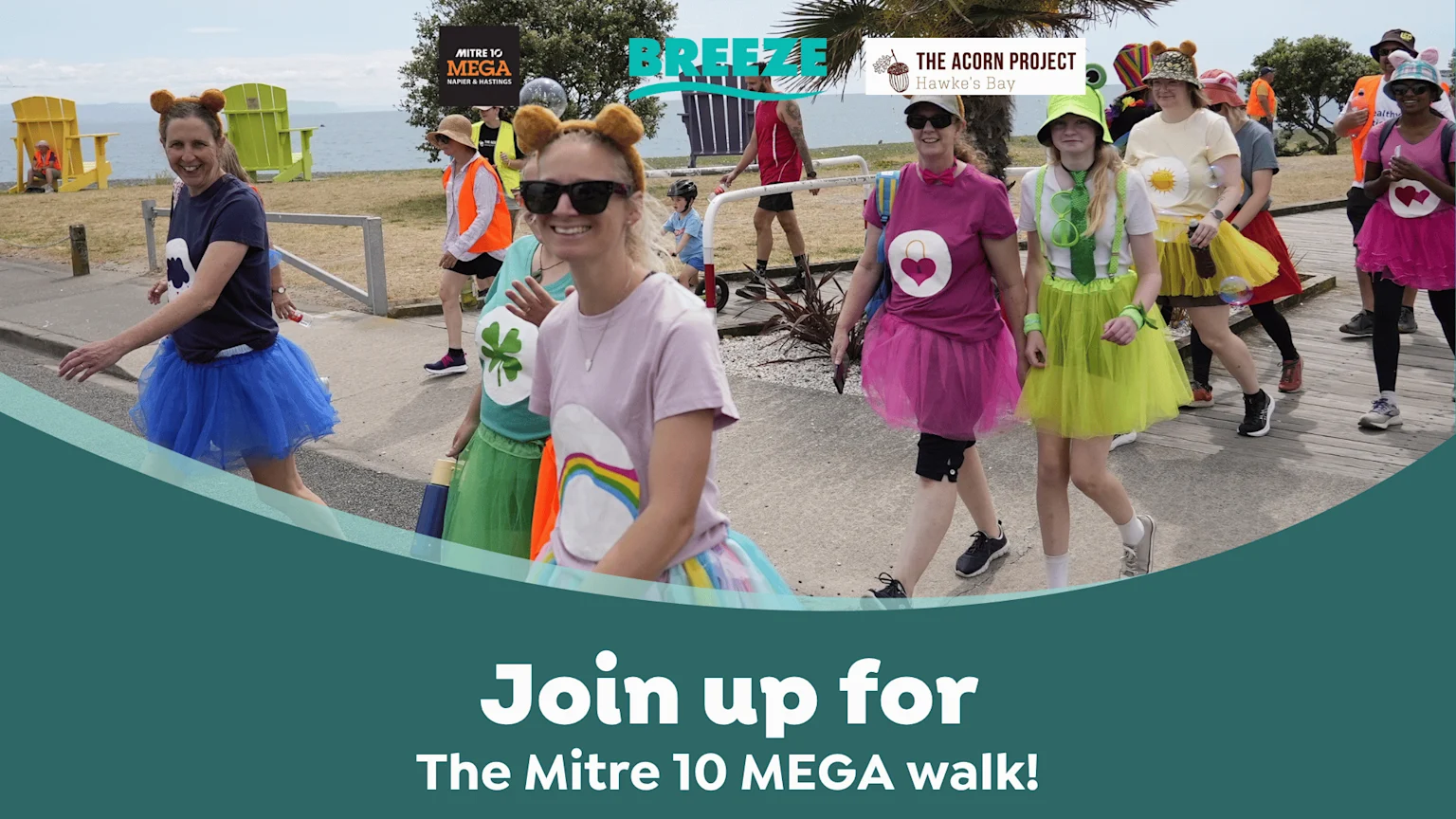 A group of smiling people, mostly women, walk outdoors dressed in colorful tutus and fun costumes, with event sponsors' logos and text "Join up for The Mitre 10 MEGA walk!" overlaid.