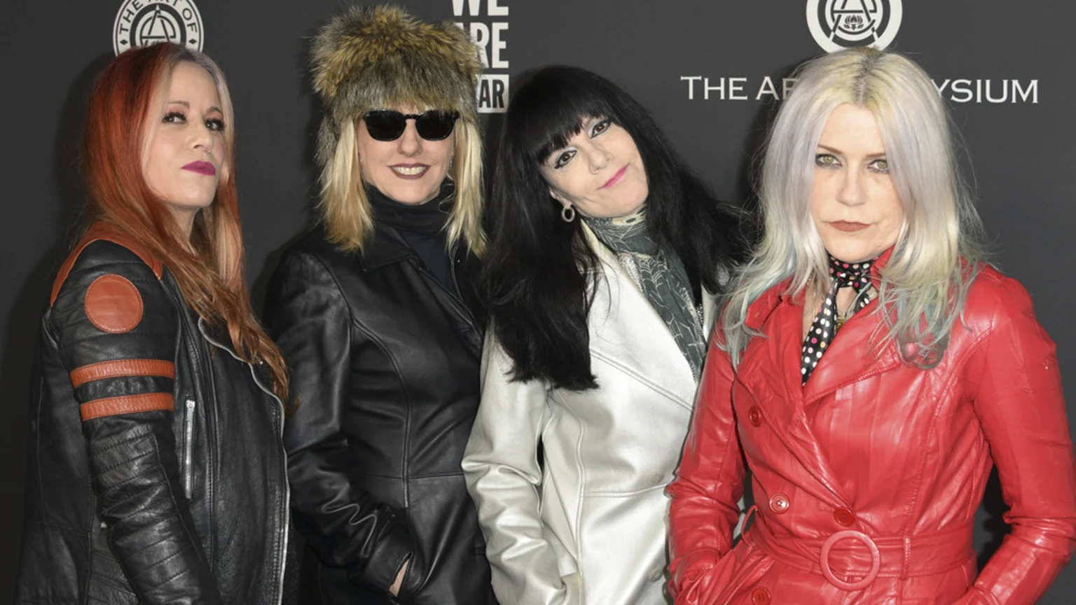 Four women, exuding a rock-and-roll style, pose together at an event, dressed in various leather jackets and coats.
