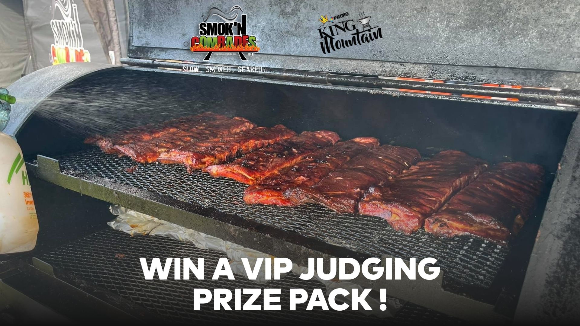 Multiple racks of ribs cook in a large black smoker, being sprayed with liquid, with "Smok'N Comrades" and "Primo King Mountain" logos above and "WIN A VIP JUDGING PRIZE PACK !" text below.