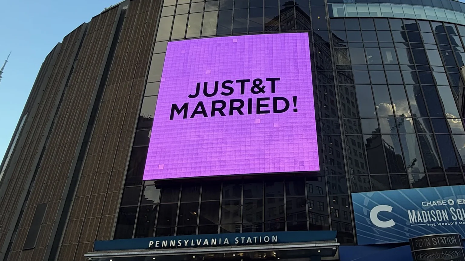 A large purple digital billboard on a building displays "JUST &T MARRIED!" above "PENNSYLVANIA STATION" and next to a "MADISON SQUARE" sign.