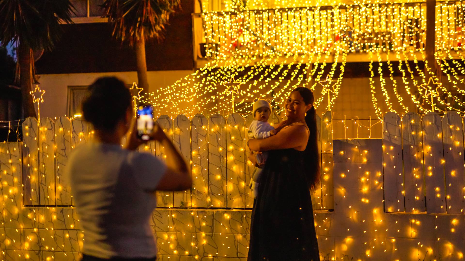 A woman and baby pose for a picture outside a house lit up with Xmas lights in Otara. 