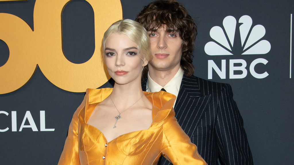 Anya Taylor-Joy in a gold dress and Malcolm McRae in a pinstripe suit pose together, with a golden "50" logo and the NBC logo visible in the background.
