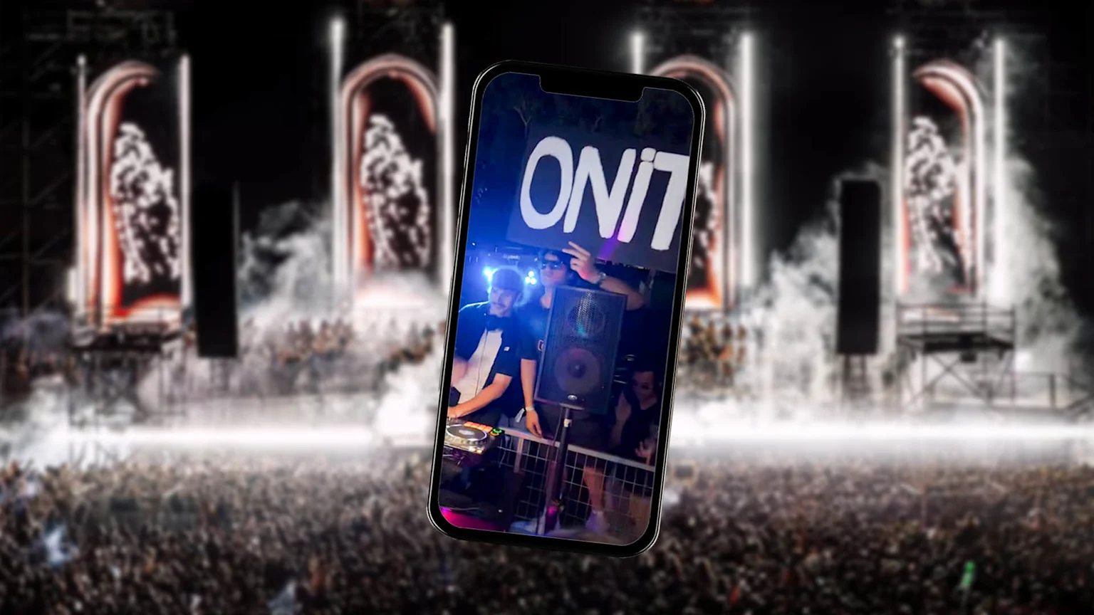 A photographic composite showing a smartphone displaying a DJ performing at an Onit Lino music festival. The phone screen features three unknown individuals near DJ equipment, one holding a sign reading 'ONIT LINO' while the blurred background reveals a large crowd, illuminated stage structures, and smoke effects at an outdoor nighttime concert.