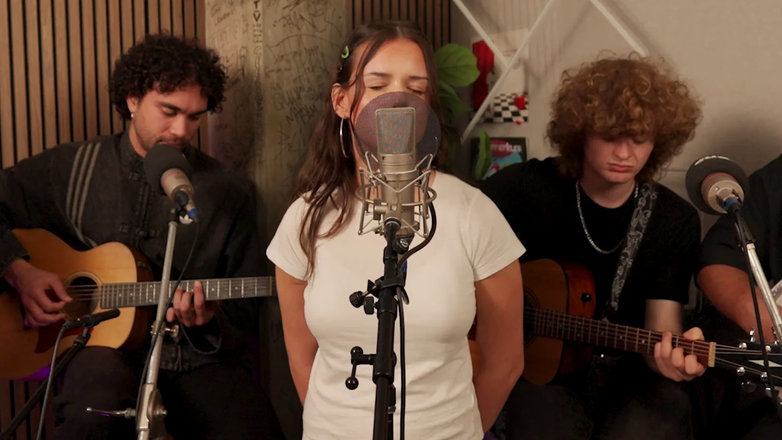 Frankie Venter sings into a microphone with a pop filter, eyes closed, flanked by two men playing acoustic guitars in a studio setting.