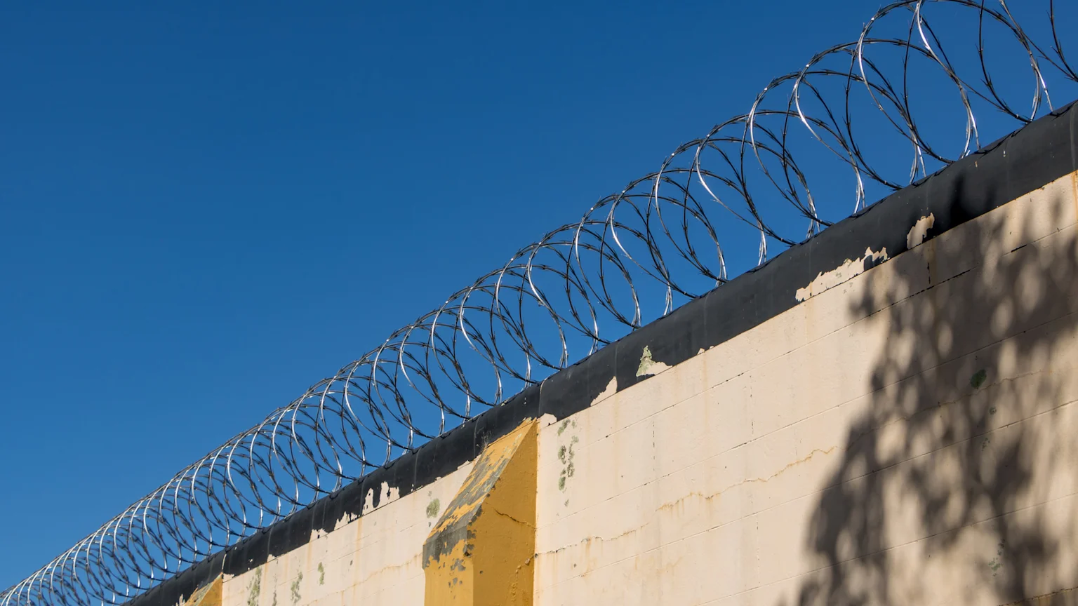 Prison wall with razor wire against blue sky