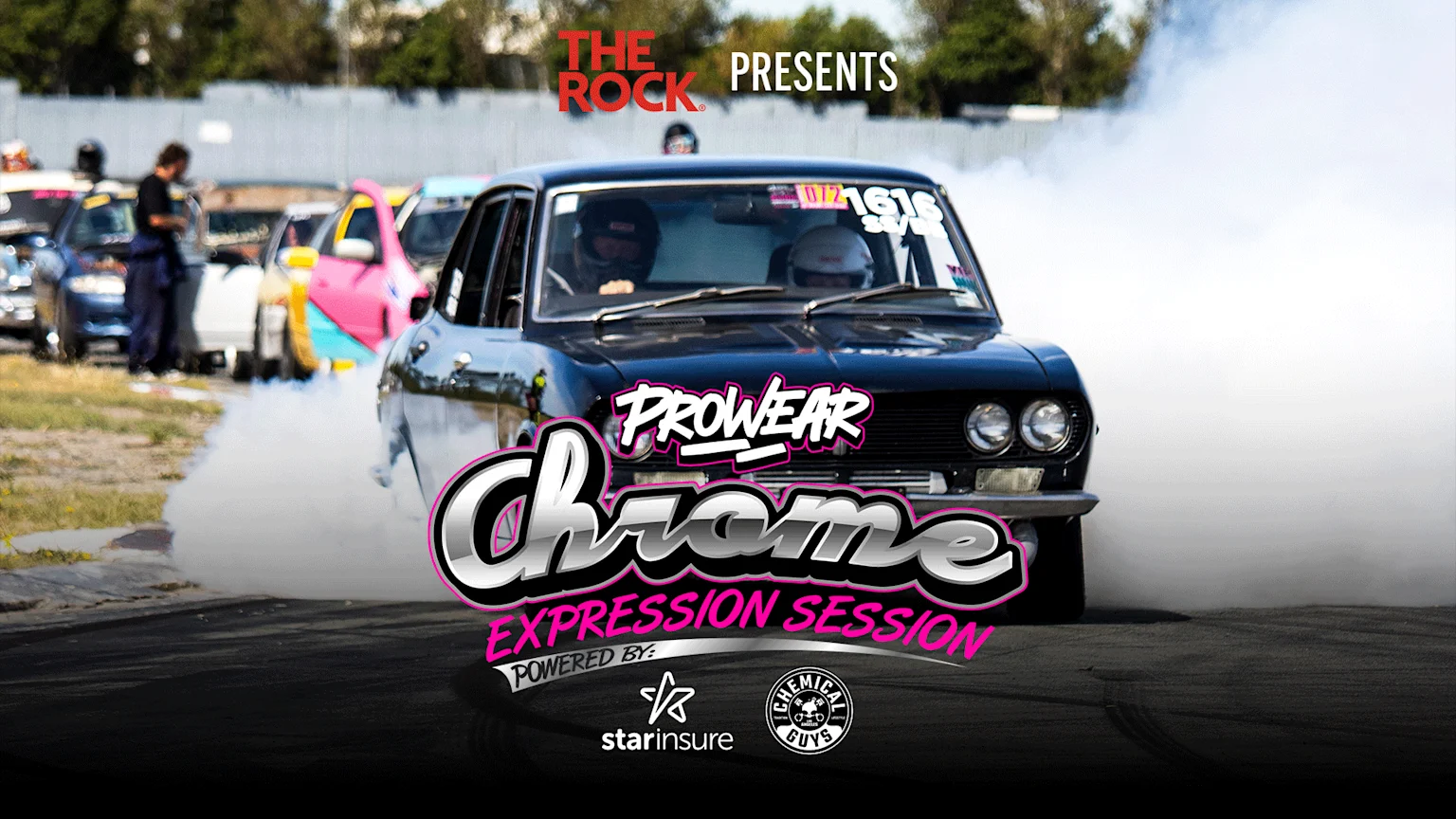 A vintage black sedan with dual round headlights performs a burnout on an outdoor asphalt racetrack, generating white smoke. Two occupants in helmets are inside, with event branding from The Rock, Starinsure, and Chemical Guys visible.