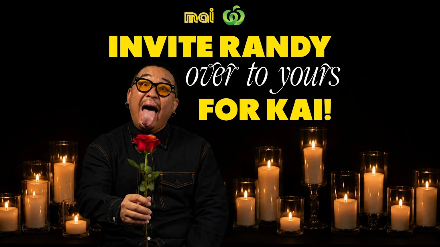 A man wearing yellow glasses with his tongue out, holding a red rose, stands amid many lit candles against a dark background, with the text "INVITE RANDY over to yours FOR KAI!" and the Mai and Woolworths logos above.