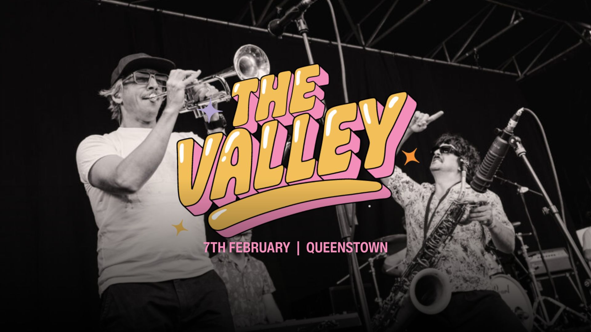 Black and white photo of two musicians on stage, one playing trumpet and another saxophone, with "THE VALLEY" in colorful bubble text overlayed, and "7TH FEBRUARY | QUEENSTOWN" below.